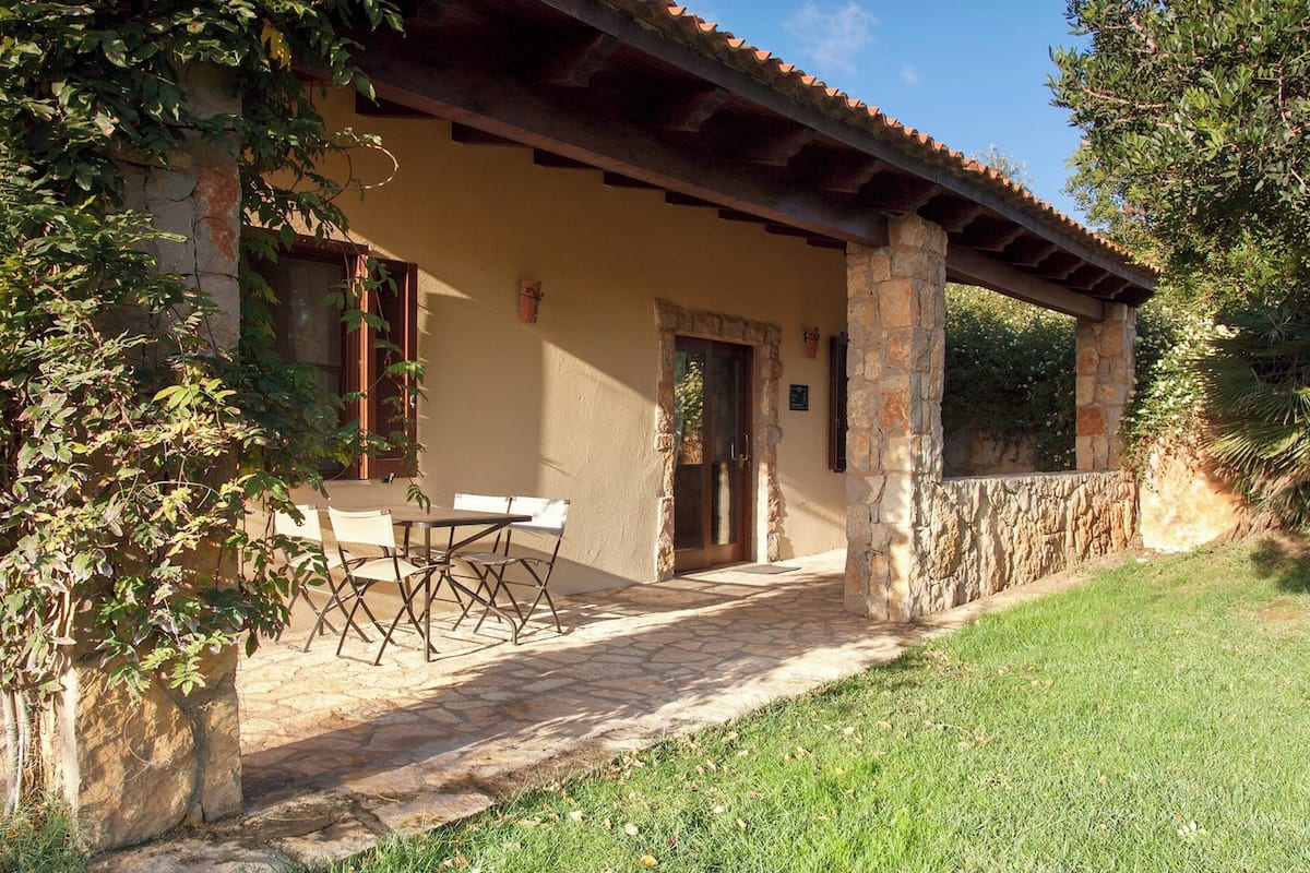 A covered patio with stone flooring, a table and chairs, and a stone wall.