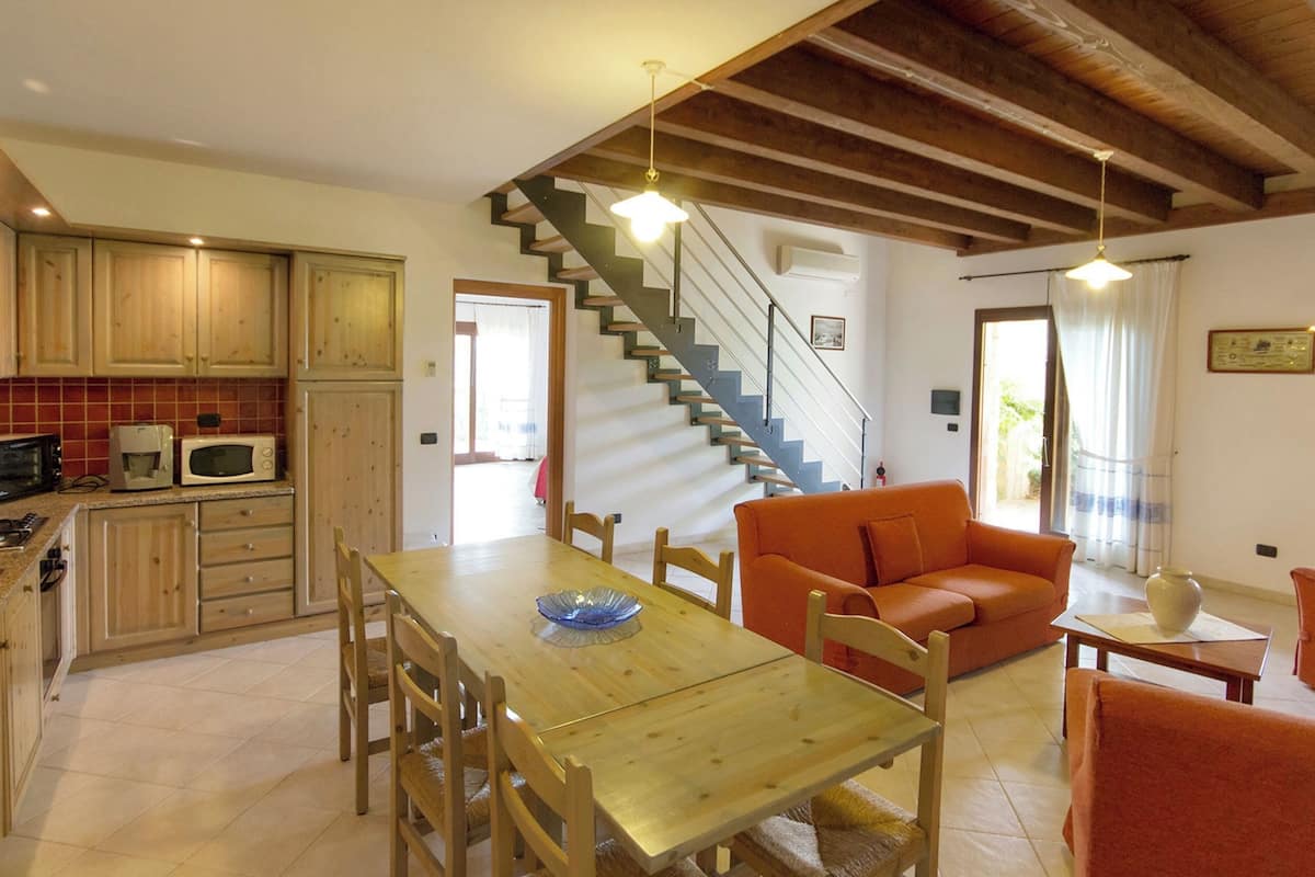 A spacious kitchen with wooden cabinets, a dining table, and a staircase leading to a balcony.