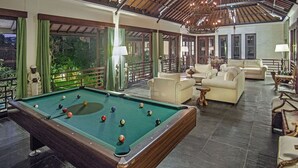 A pool table in a well-lit room with multiple seating areas and large windows offering views of greenery. - Villa Avalon I by Elite Havens (Kabupaten Badung)