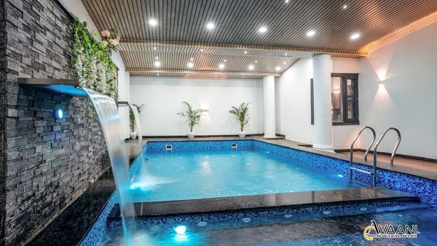 An indoor swimming pool with a stone wall, a wooden ceiling, and a small waterfall feature. - Avaani Residency ,A Spacious 5-bedroom villa in beautiful Jalandhar with AC (Jalandhar)