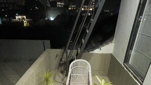 A balcony with two white wicker chairs, a small round table, and several potted plants. - Avaani Residency ,A Spacious 5-bedroom villa in beautiful Jalandhar with AC (Jalandhar)