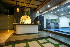 A modern bar area with a central bar, decorative lighting, and a small water feature.