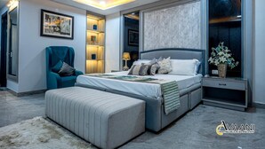 A modern bedroom with a large bed, a chair, a nightstand, and a wall-mounted TV. - Avaani Residency ,A Spacious 5-bedroom villa in beautiful Jalandhar with AC (Jalandhar)