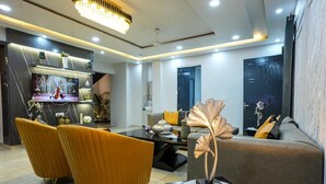 A modern living room with a dining area, featuring a chandelier, a flat-screen TV, and a sofa with decorative pillows. - Avaani Residency ,A Spacious 5-bedroom villa in beautiful Jalandhar with AC (Jalandhar)