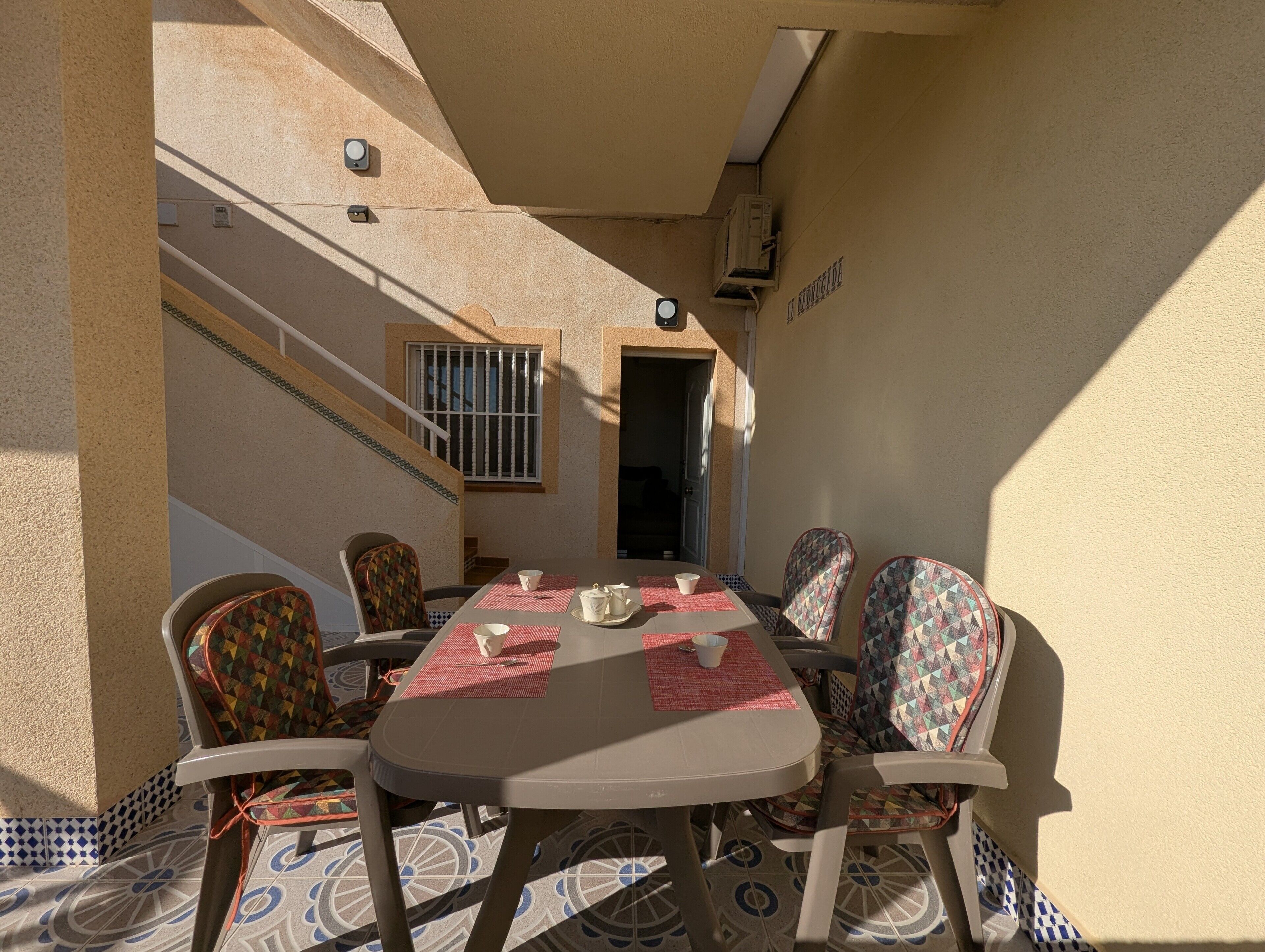 A sunlit outdoor dining area with a table, chairs, and a staircase.