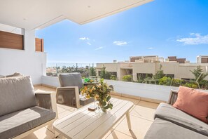 Un balcón moderno con sofá, sillones y una mesa de centro, con vistas a un paisaje urbano.