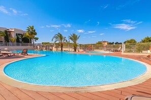A swimming pool with a wooden deck, lounge chairs, and palm trees. - Lotus Jardinana Paradise (Mijas)