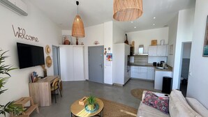 A modern living room with a sofa, coffee table, and a TV mounted on the wall. There is a kitchen area with cabinets and a microwave. - Beautiful seaside apartment with pool (Ajaccio)