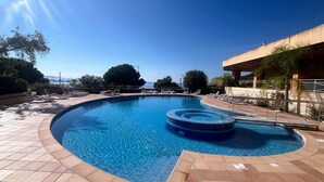 A swimming pool with a circular hot tub, surrounded by lounge chairs and a tiled deck. - Beautiful seaside apartment with pool (Ajaccio)