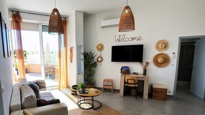 A modern living room with a sofa, coffee table, TV, and a desk with a chair. - Beautiful seaside apartment with pool (Ajaccio)