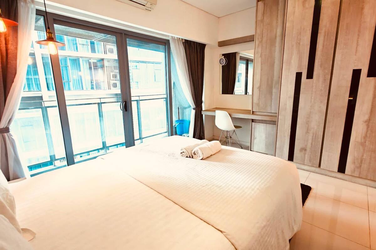 Quarto de hotel com uma cama grande, uma escrivaninha, uma cadeira, um espelho e vista para o exterior.