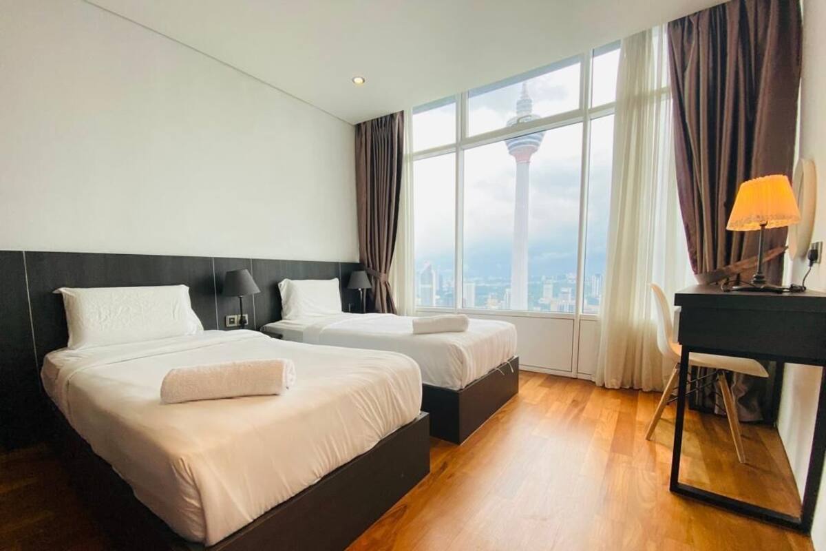 Quarto de hotel com duas camas, uma escrivaninha e uma janela grande com vista para a cidade.