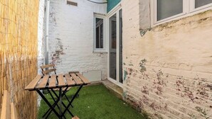 A small outdoor patio with a wooden table and chairs, a green artificial turf area, and a white brick wall. - Ravissante New 3 chambres à Roubaix (Roubaix)