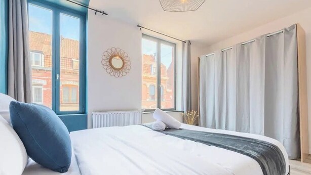 A modern bedroom with a large bed, a view of buildings through the window, and a radiator on the wall. - Ravissante New 3 chambres à Roubaix (Roubaix)