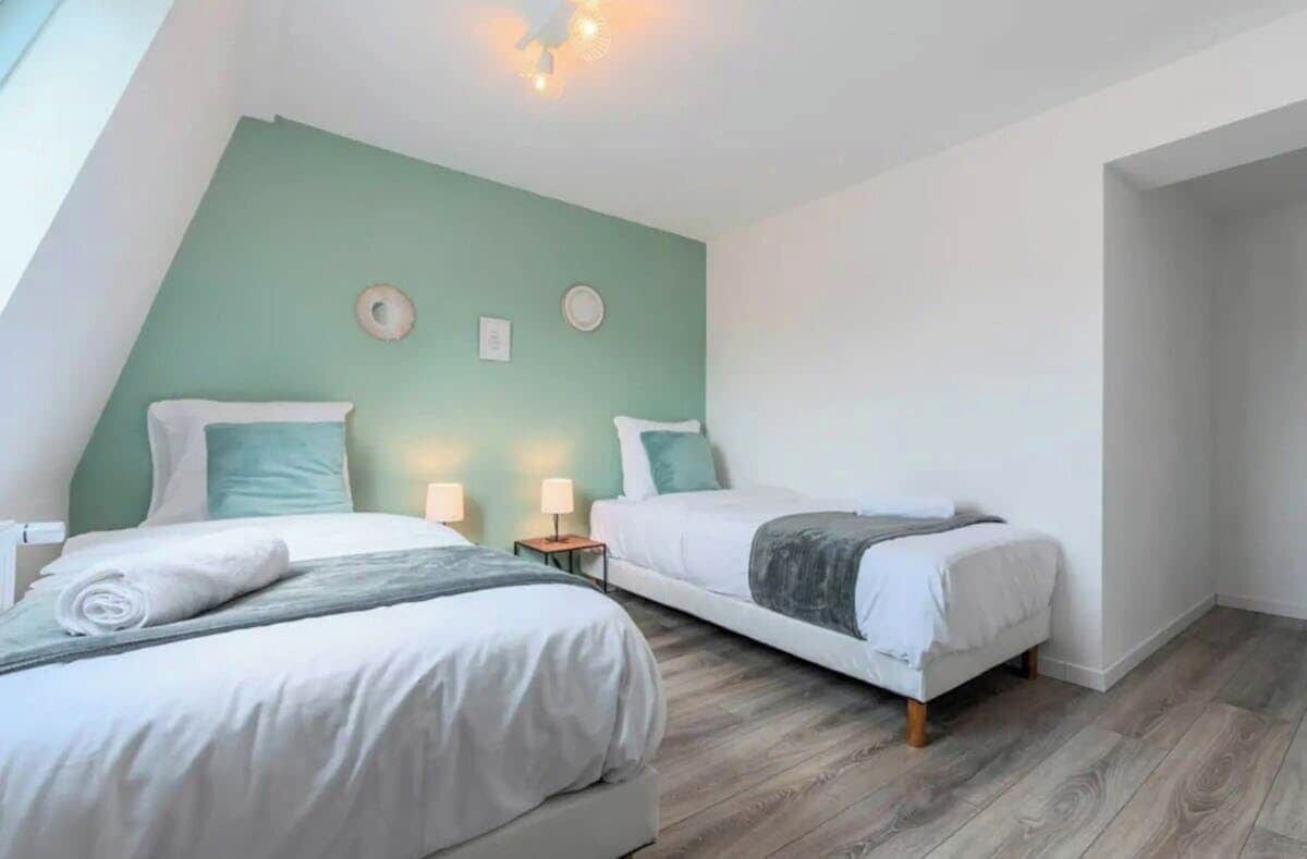 A bedroom with two beds, a green accent wall, and a wooden floor.