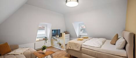 A spacious loft bedroom with a large bed, a sofa, a wooden coffee table, and a small desk.