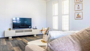 Un salon moderne avec un téléviseur à écran plat posé sur un meuble de télévision blanc, un canapé et une fenêtre équipée de stores.