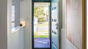 Un couloir avec une porte donnant sur l’extérieur, une fenêtre avec des stores et une lampe fixée au mur.