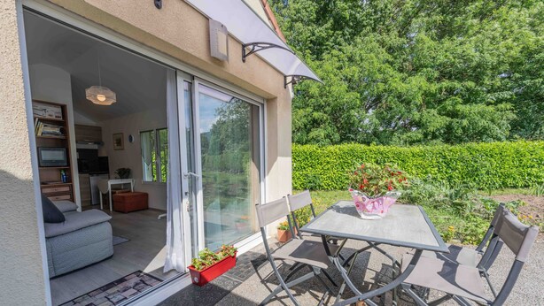 A modern outdoor patio with a table and chairs, a sliding glass door leading to an interior space, and a garden view.