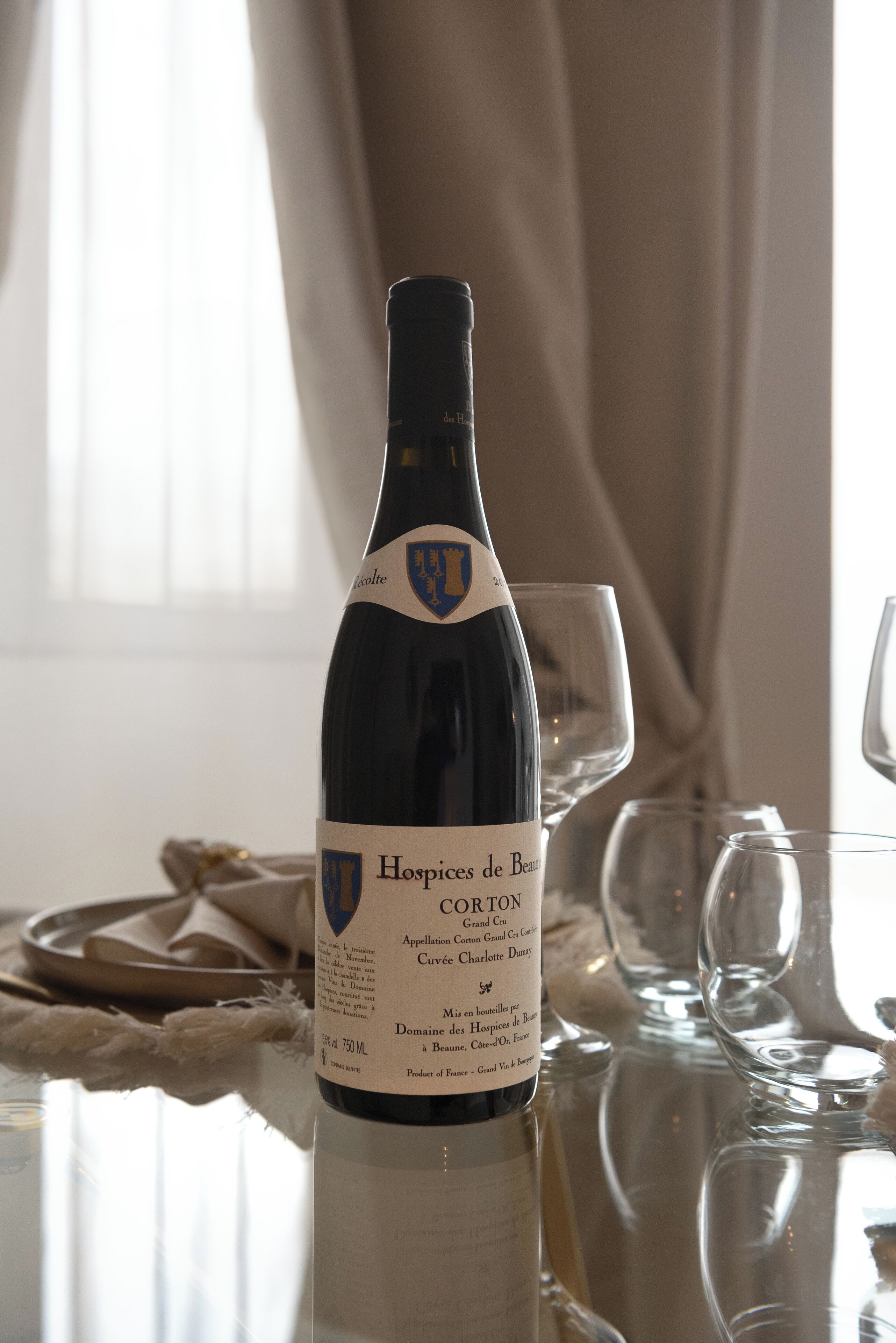 A bottle of Hospices de Beaune CORTON wine on a table with empty wine glasses.
