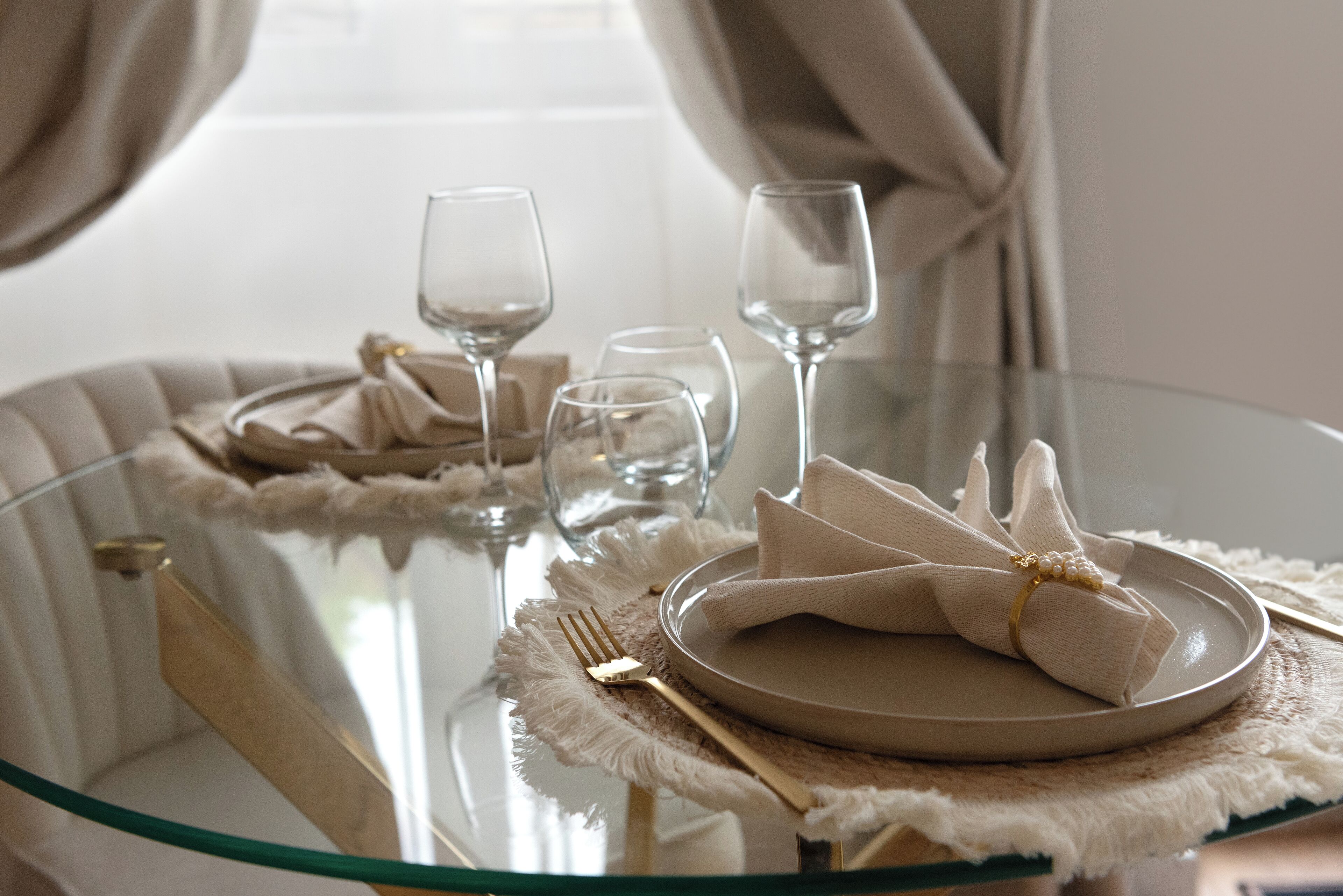 Een eettafel met een glazen blad, gedekt met een bord, servet, vork en wijnglazen.