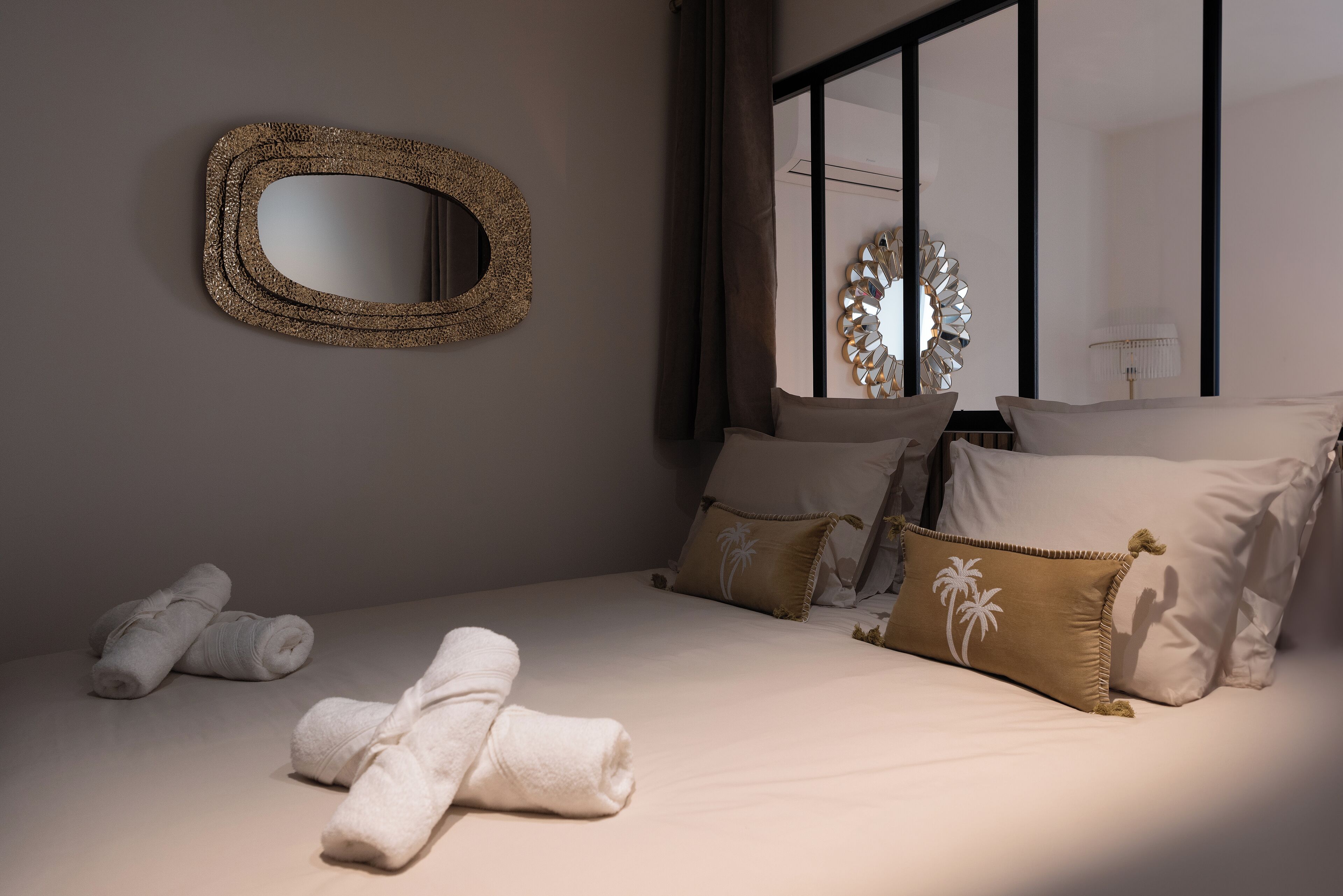 Cama bem arrumada com toalhas, um espelho grande e arte decorativa nas paredes em um quarto moderno.