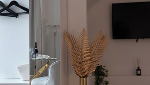 A modern room with a glass dining table, a white chair, a tall vase with dried foliage, and a mounted TV. - Les Nuits en Grands Crus Cosy apartment near Beaune, in the heart of the vineyards  (Ladoix-Serrigny)