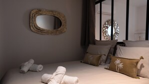 A neatly made bed with rolled towels, a decorative mirror, and palm tree pillows. - Les Nuits en Grands Crus Cosy apartment near Beaune, in the heart of the vineyards  (Ladoix-Serrigny)