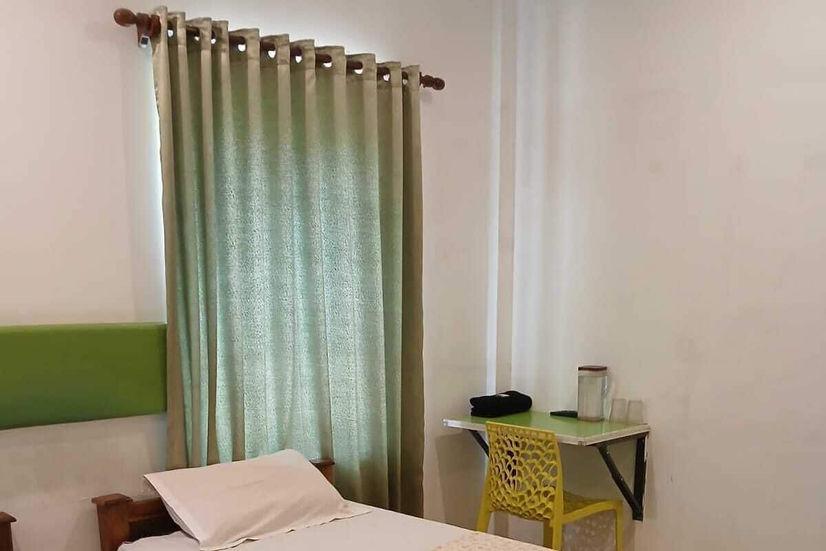 A room with two wooden beds, a green curtain, a small table with a yellow chair, and a white wall.