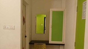 A narrow hallway with a green door, a small desk with a chair, and a mirror on the wall. - Spring Valley Hotels (Thiruvananthapuram)