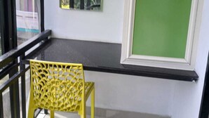 A balcony with a yellow chair, a green screen, and a window with a view of trees. - Spring Valley Hotels (Thiruvananthapuram)