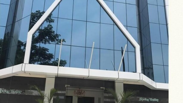 A modern building with a glass facade and a distinctive white arch structure at the entrance. - Spring Valley Hotels (Thiruvananthapuram)