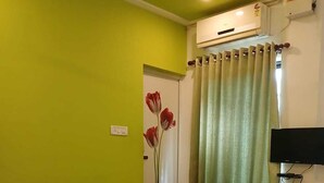 A room with a bed, an air conditioning unit, a television, and a door with a floral decoration. - Spring Valley Hotels (Thiruvananthapuram)