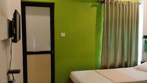 A room with two single beds, a ceiling fan, an air conditioning unit, a television mounted on the wall, and a door with a black frame. - Spring Valley Hotels (Thiruvananthapuram)