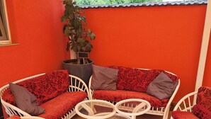Un espace extérieur accueillant, aménagé avec des meubles en osier et des coussins rouges, une plante en pot et un sol carrelé.