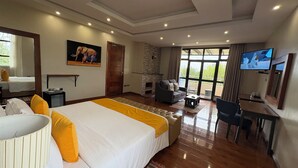 Ein geräumiges Hotelzimmer mit einem großen Bett, einer Sitzecke mit einer Couch und Sesseln, einem Fernseher und einem Kamin.