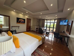Une chambre d’hôtel spacieuse, dotée d’un grand lit, d’un coin salon avec un canapé et des fauteuils, d’une télévision et d’une cheminée.