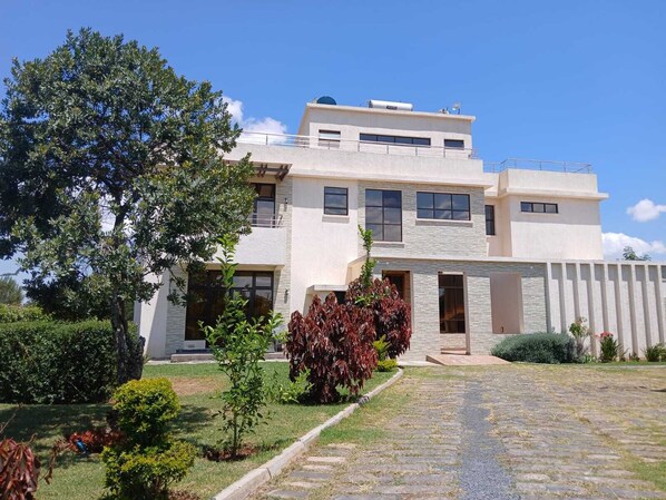 A modern two-story house with a stone facade, large windows, and a well-maintained garden with various plants and a paved driveway.