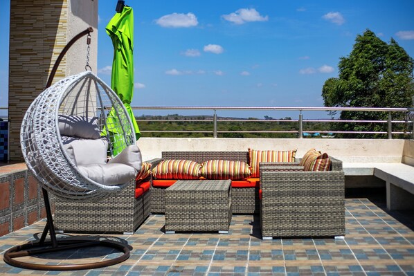 An outdoor seating area with wicker furniture, a hanging chair, and a green umbrella.