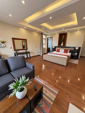 A modern hotel room with a sofa, a bed with a headboard, a mirror, and a small table with a vase of flowers.