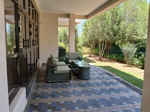 Un patio couvert aménagé avec du mobilier d’extérieur, notamment un canapé et des fauteuils, ainsi qu’une table.