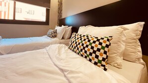A hotel room with two beds, white bedding, a window with a view of buildings, and a dark headboard. - Relax family Élysée (Ouarzazate)