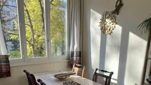 Ruokailutila, jossa on pöytä ja tuolit, ikkuna, jossa on verhot, sekä koristeellinen seinävaate.