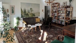Olohuoneessa on sohva, nojatuoleja, sohvapöytä, kirjahylly ja suuri taulu seinällä.
