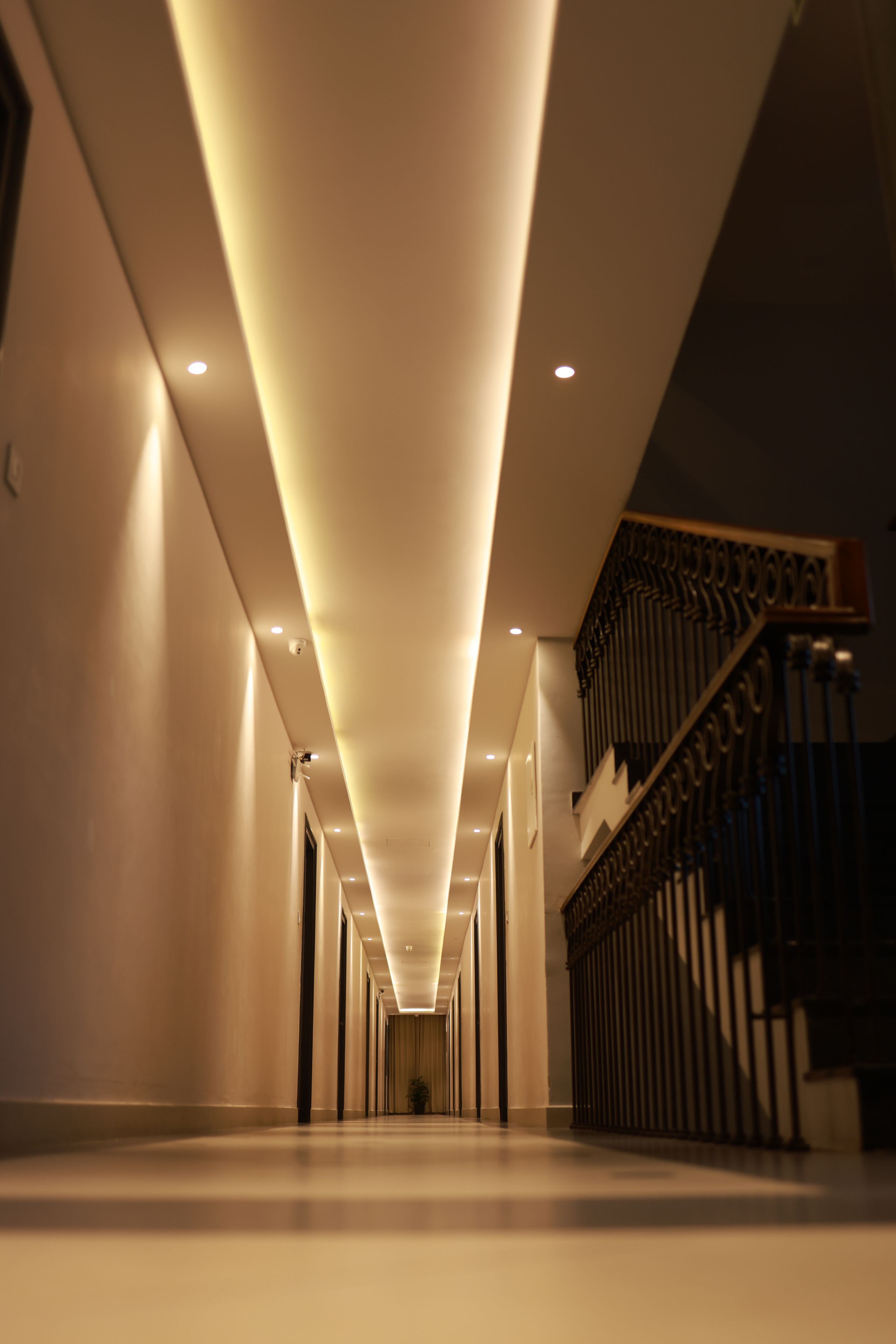 Un long couloir étroit au design moderne, avec un escalier sur le côté droit agrémenté d’une rampe décorative.