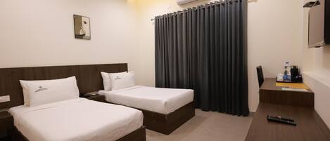 A hotel room with two beds, a desk, a chair, a TV, and an air conditioning unit.