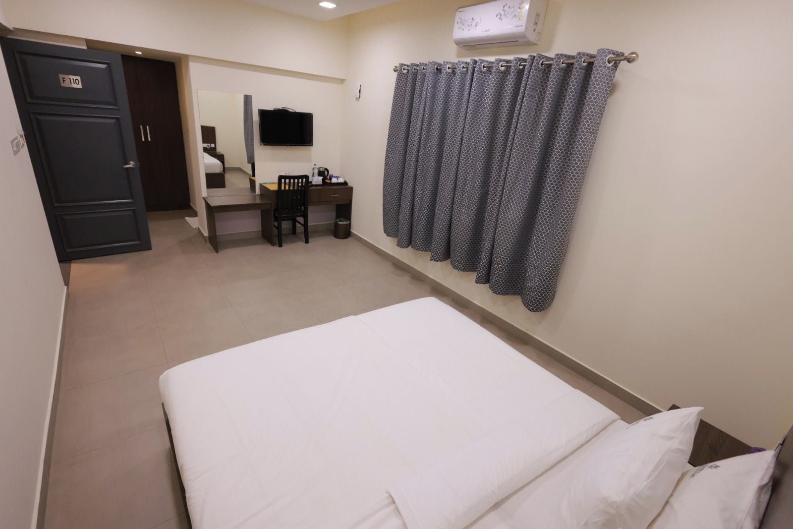 A hotel room with a bed, a desk with a chair, a television, and a wardrobe.
