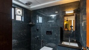 Un baño moderno con paredes de mármol oscuro, un inodoro blanco, un lavabo y una zona de ducha.