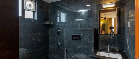 A modern bathroom with dark marble walls, a white toilet, a sink, and a shower area.