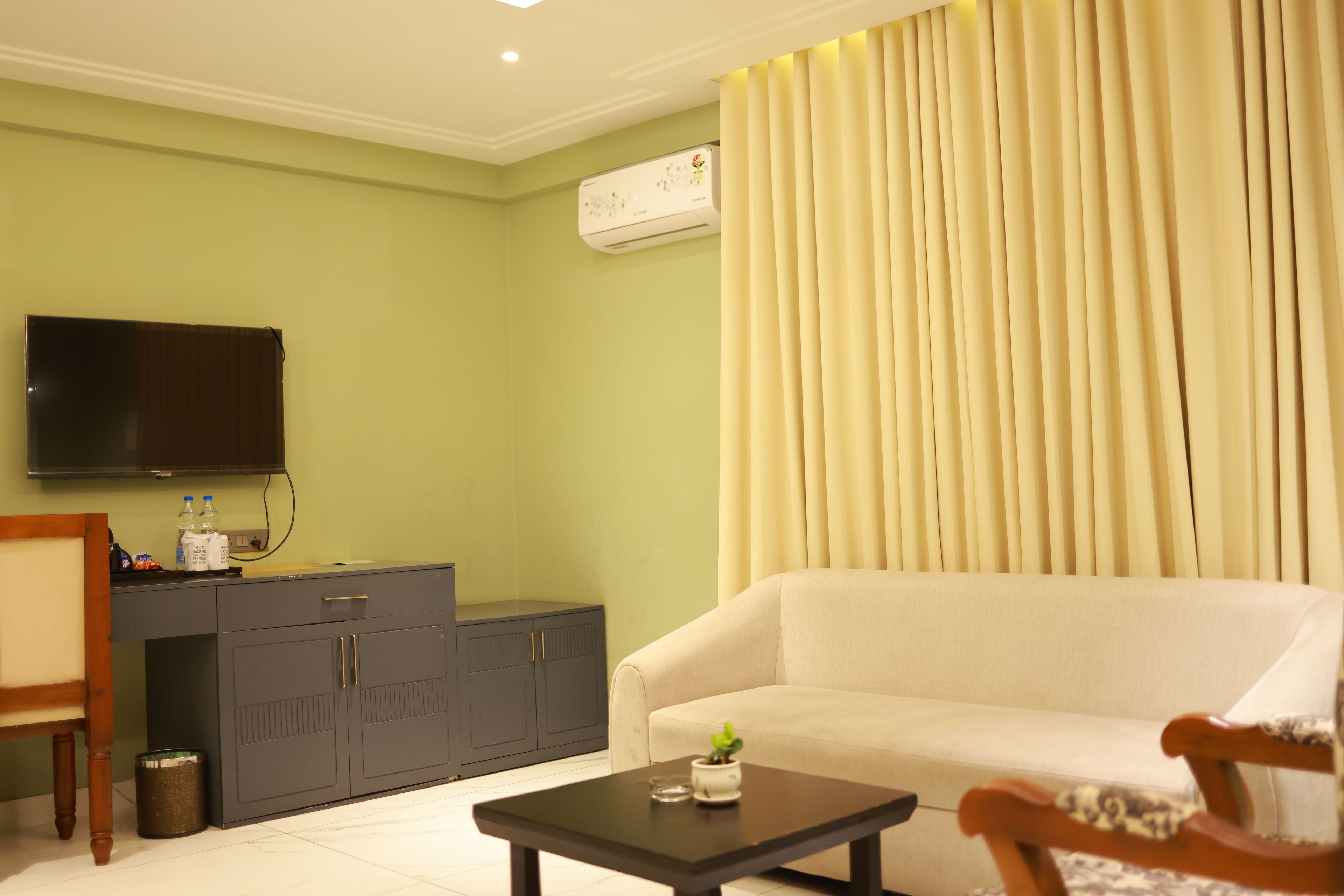 A living room with a sofa, a coffee table, a television mounted on the wall, a cabinet, and a curtain.